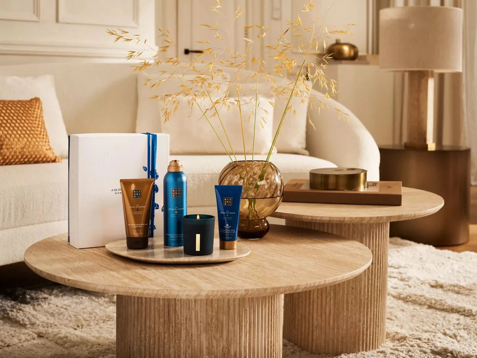 The Ritual of Hammam zestaw upominkowy Rituals z kosmetykami i świecą na drewnianym stoliku w salonie