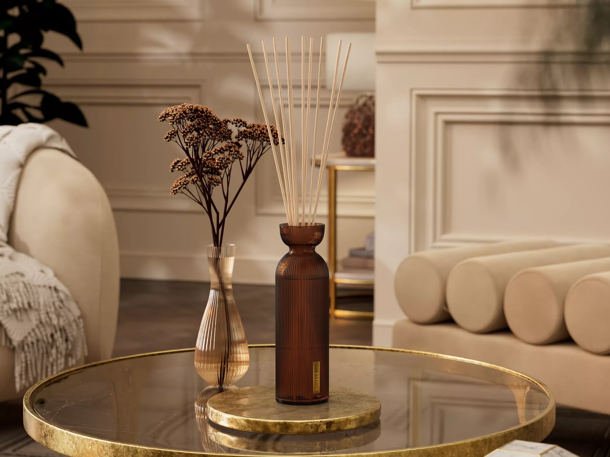 Aromatyczne patyczki do firmy Rituals w eleganckim brązowym flakonie na szklanym stole w salonie