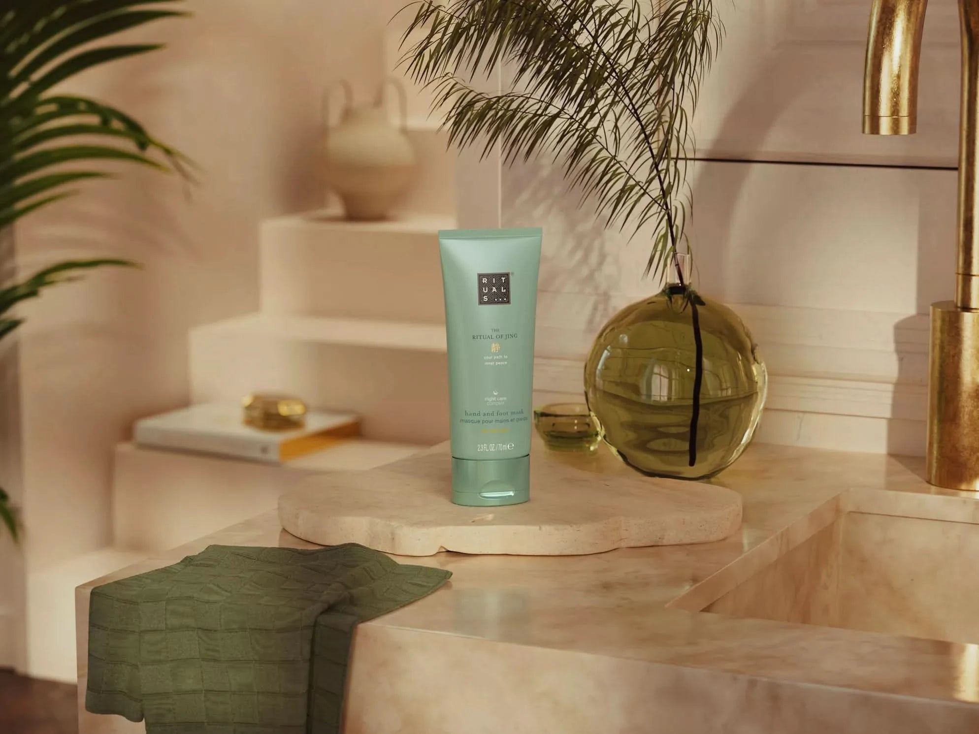 Balsam do rąk Rituals w zielonej tubce na łazienkowej półce obok doniczki i ręcznika