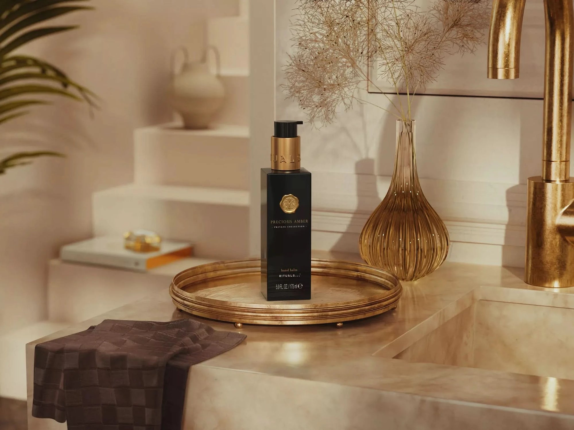 Balsam do rąk Rituals Precious Amber w eleganckim czarnym opakowaniu na mosiężnej tacy przy umywalce