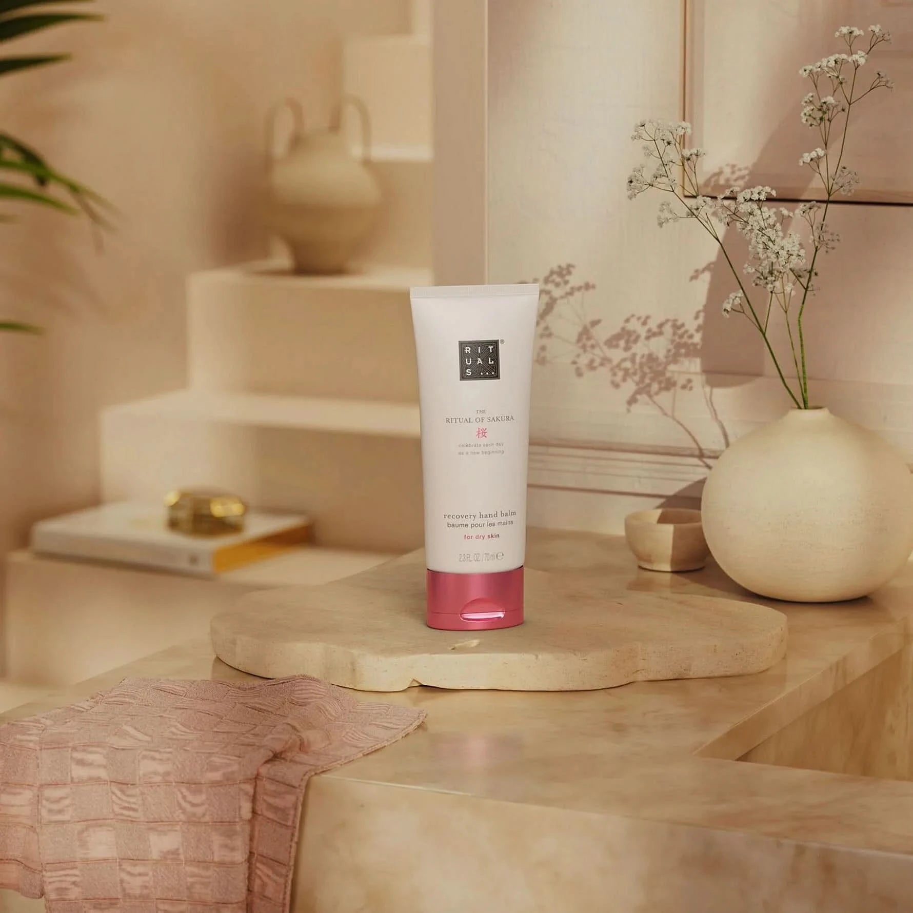 Rituals balsam do rąk sakura w białej tubce z różową nakrętką na łazienkowej półce z dekoracją