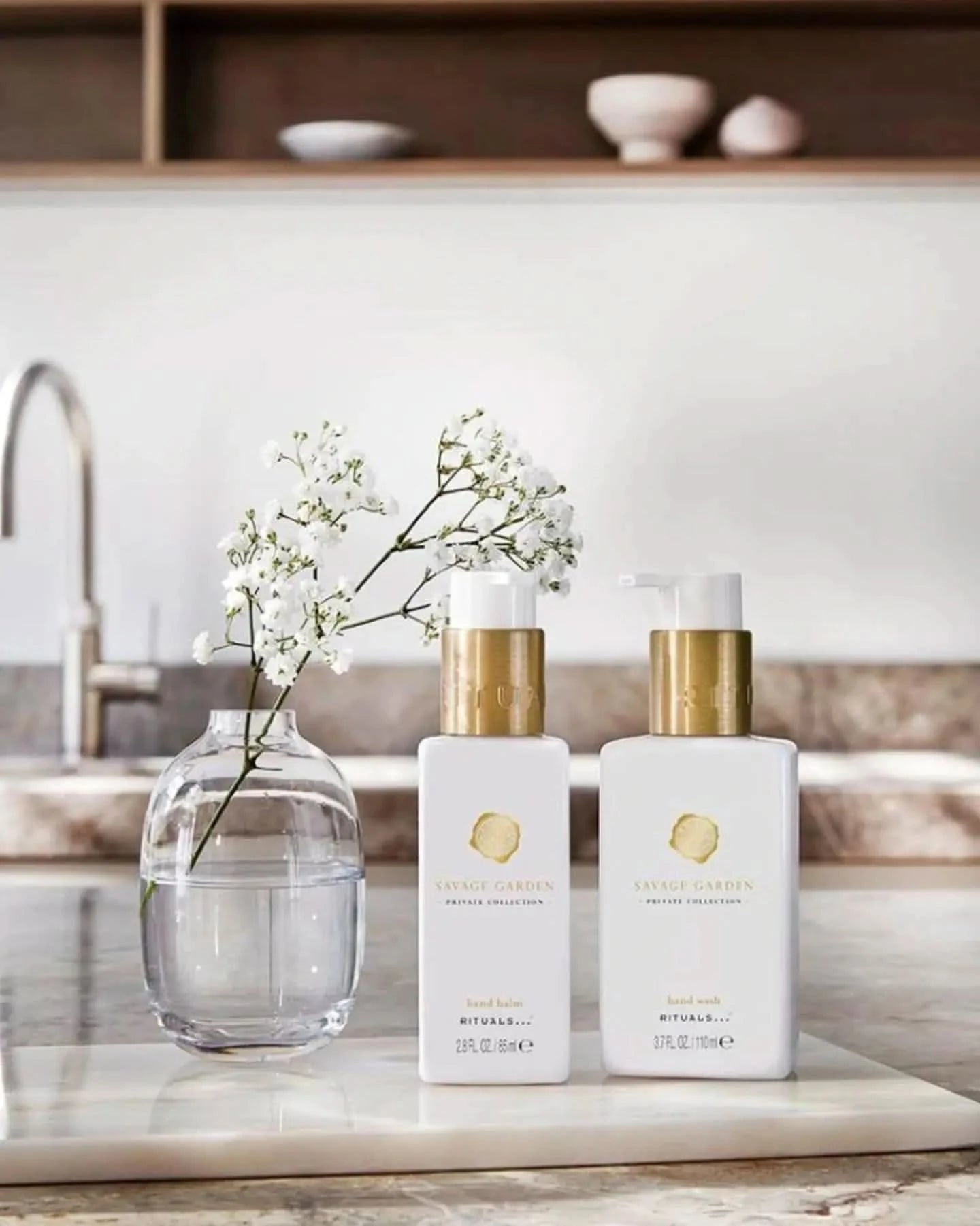 Rituals mini zestaw dla firm z dwoma białymi butelkami kosmetyków i wazonem z kwiatem na marmurowym blacie