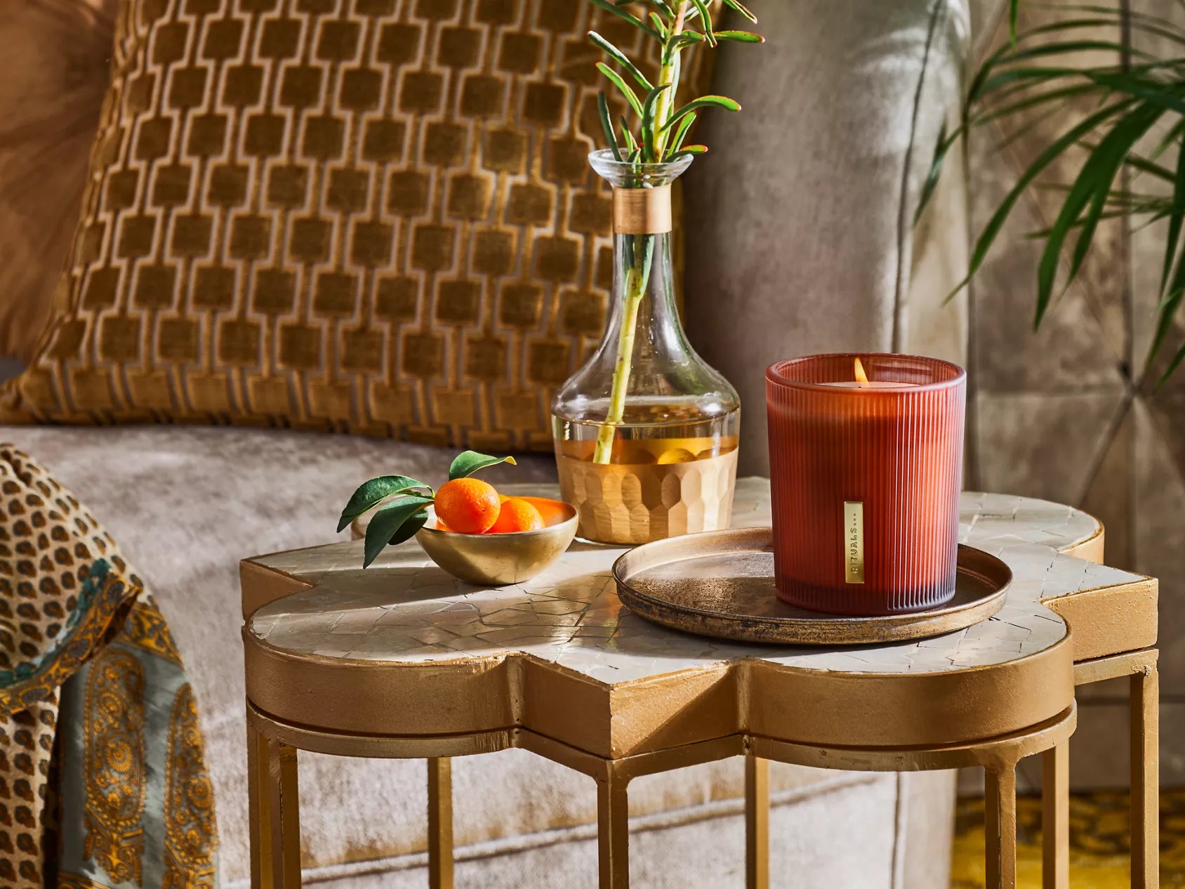 Świeca zapachowa Rituals The Ritual of Mehr na stoliku obok dekoracyjnej butelki i miski z owocami