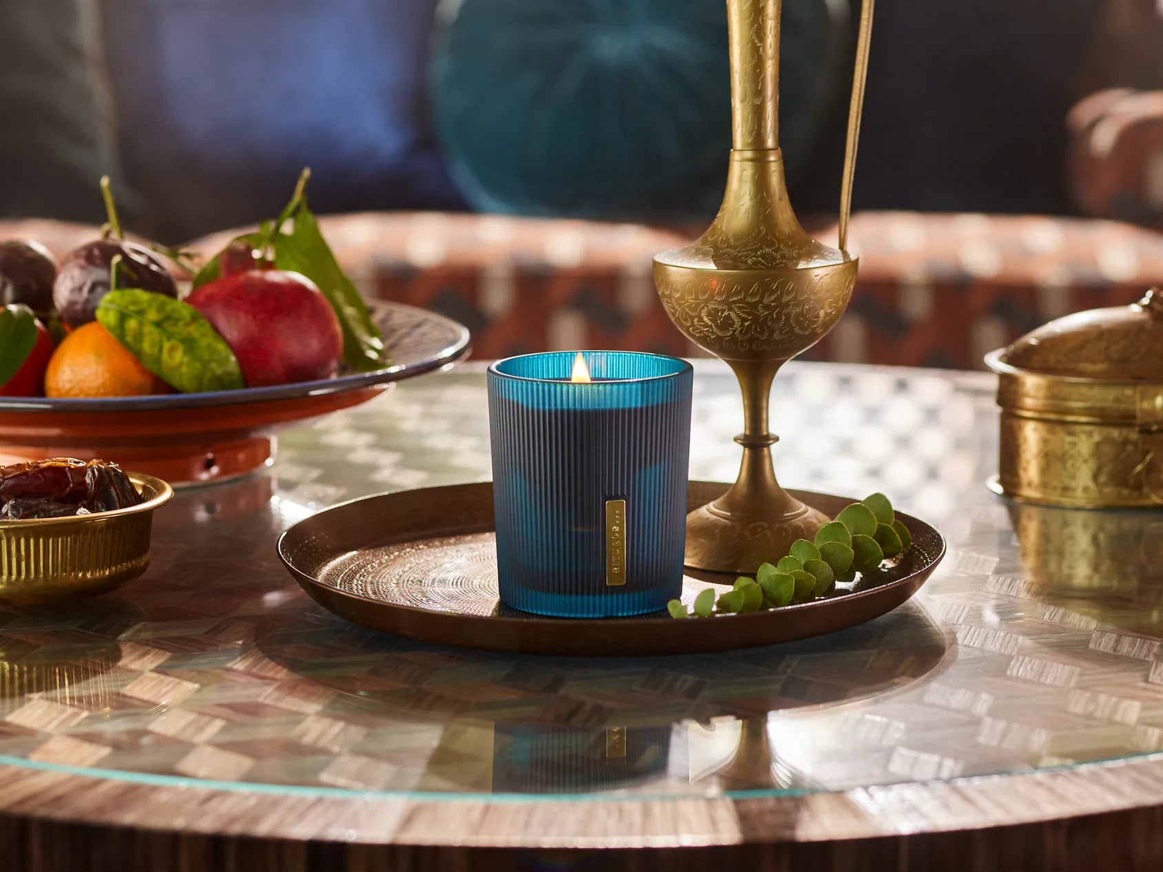 Niebieska świeca zapachowa Rituals Hammam na miedzianej tacy na stole z owocami i mosiężnymi dekoracjami
