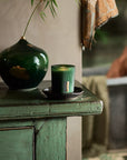 Świeca zapachowa Rituals Jing w zielonym szklanym pojemniku na drewnianym blacie łazienkowym