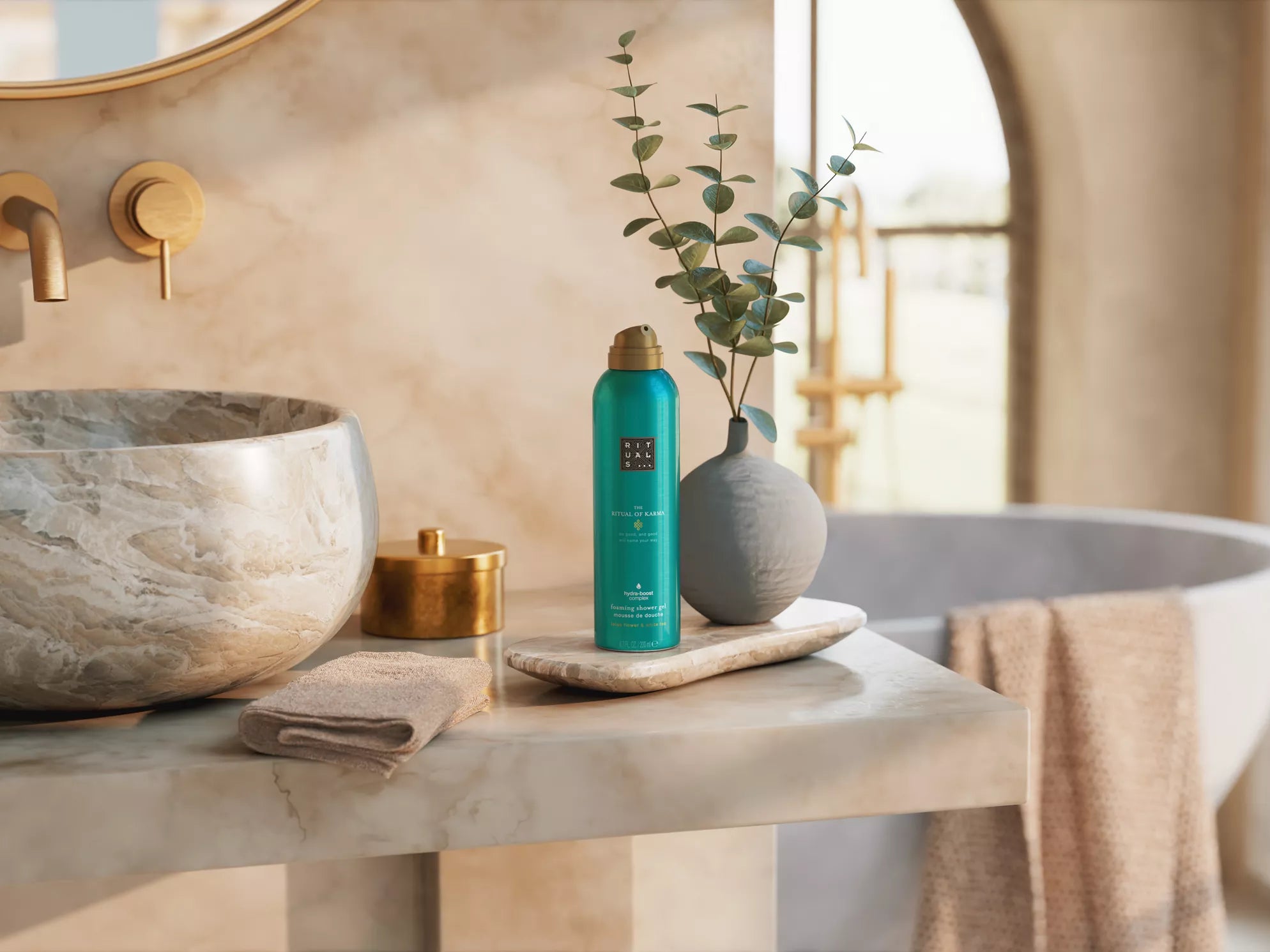 Rituals The Ritual of Karma żel do mycia w zielonym opakowaniu ustawiony na łazienkowym blacie z kamienną umywalką i dekoracyjną rośliną