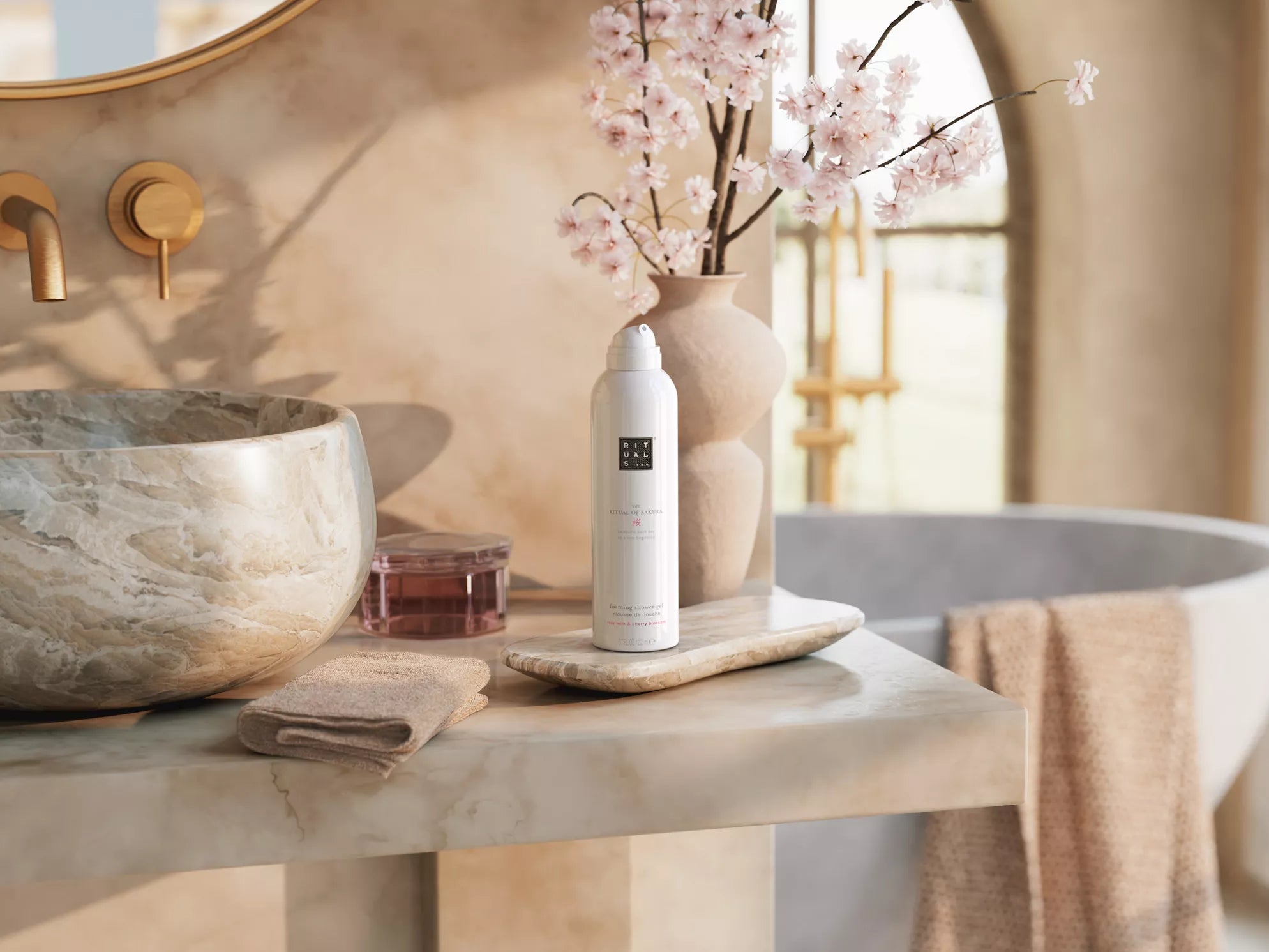 Rituals żel do mycia ciała Sakura w formie pianki obok kwiatów sakury na kamiennym blacie w łazience