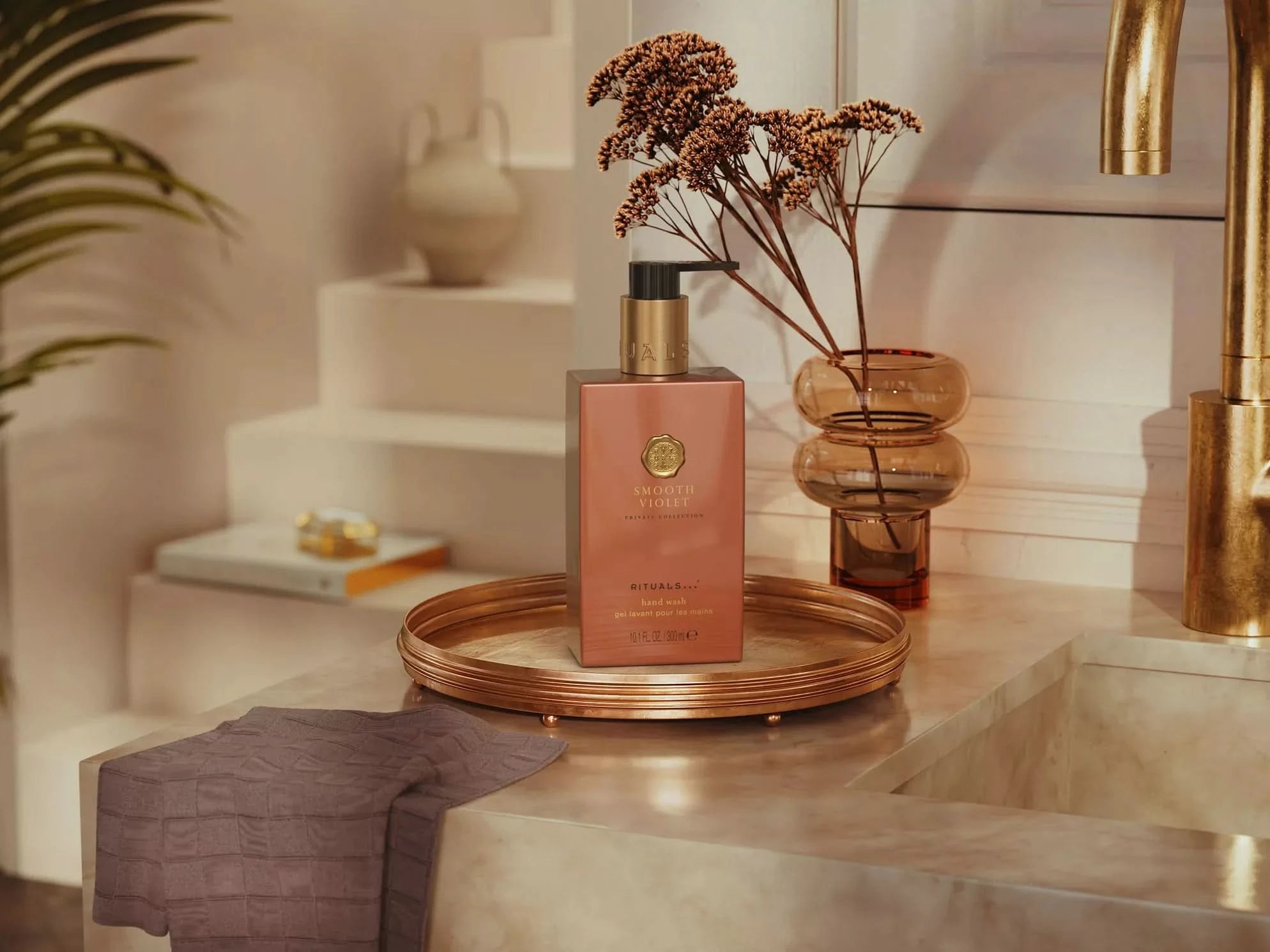 Żel do mycia rąk Smooth Violet marki Rituals na złotej tacy obok suszonych kwiatów