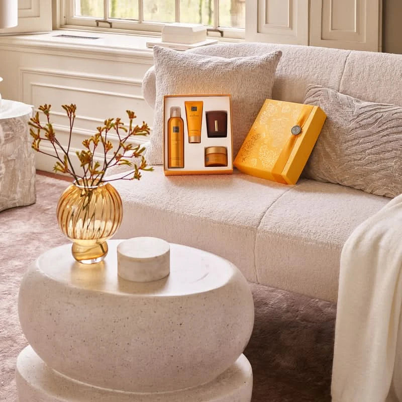 Zestaw prezentowy Rituals Mehr dla firm na kanapie w eleganckim pomarańczowym opakowaniu z kosmetykami