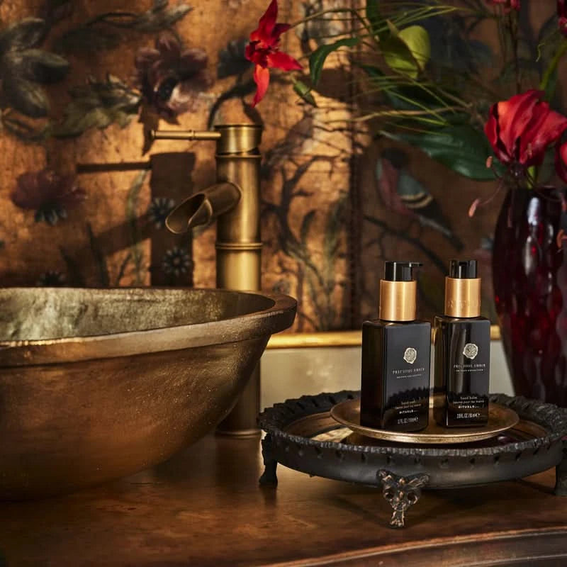 Elegancki zestaw prezentowy Rituals Precious Amber z dwoma kosmetykami na złotej tacy przy mosiężnej umywalce