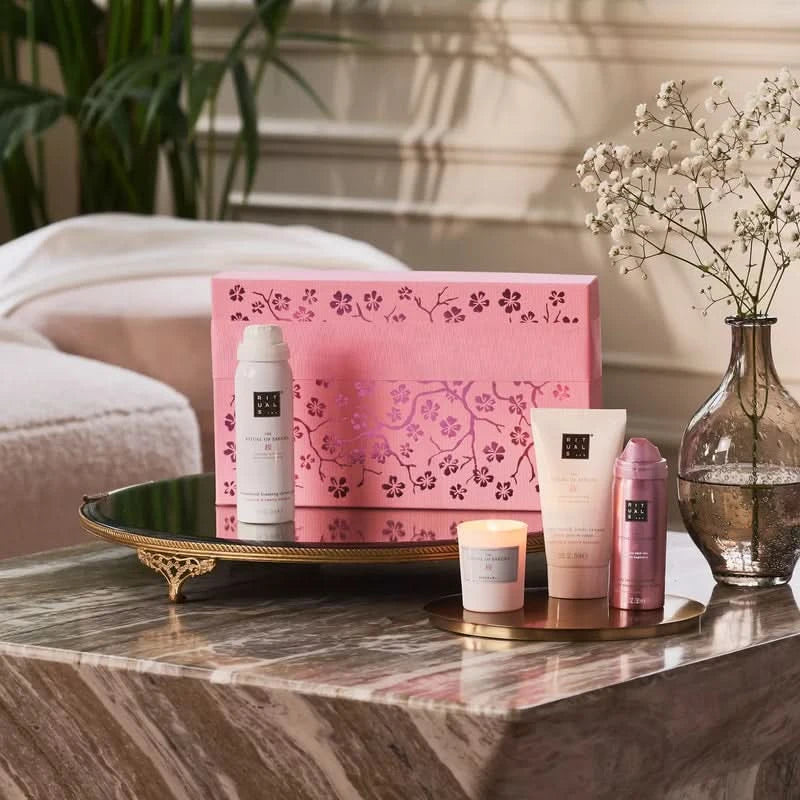 Zestaw prezentowy Rituals Sakura dla firm z kosmetykami i świecą w różowym opakowaniu na marmurowym stole