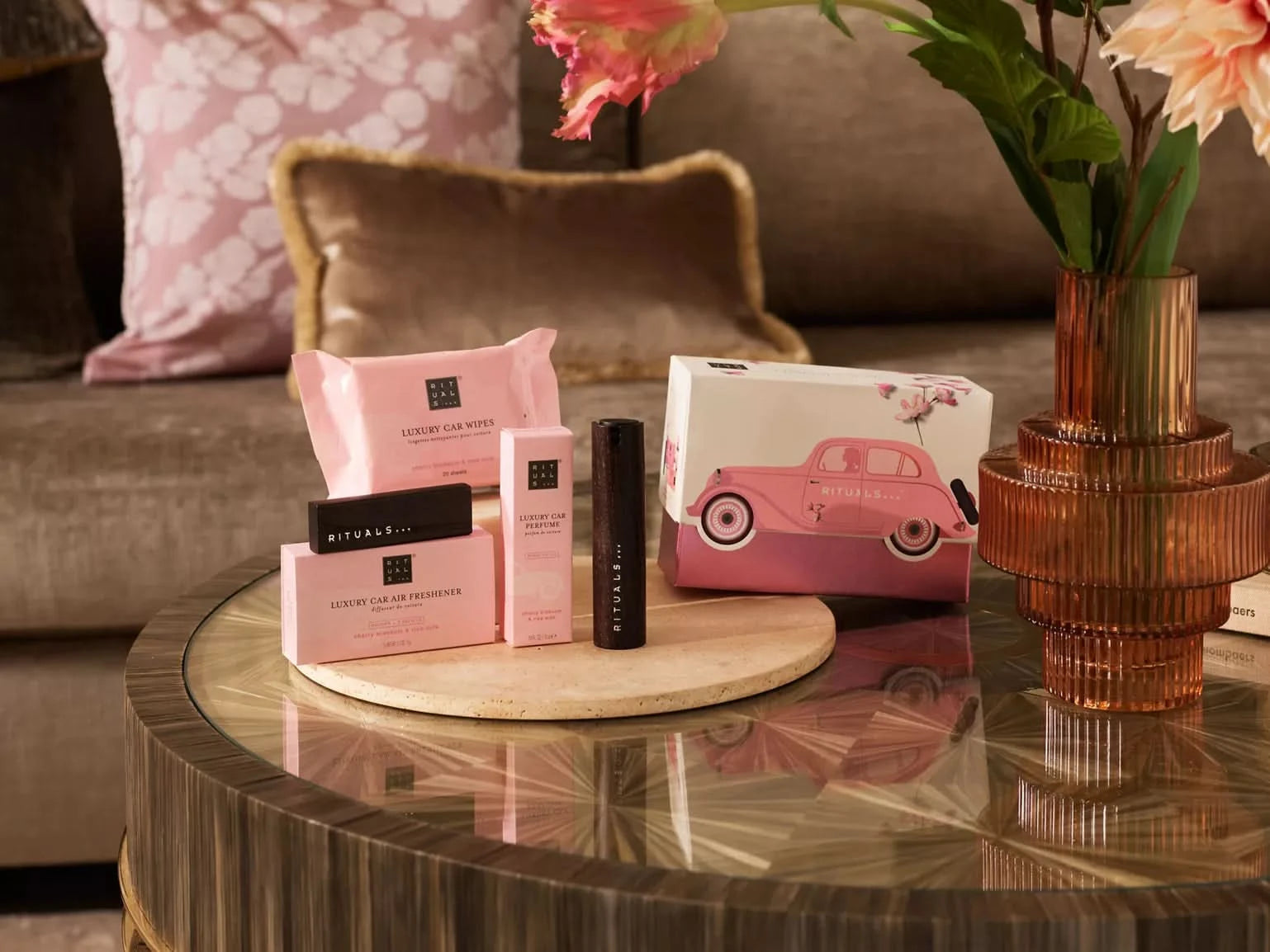 Zestaw upominkowy do samochodu Rituals z różowymi produktami pielęgnacyjnymi na szklanym stole