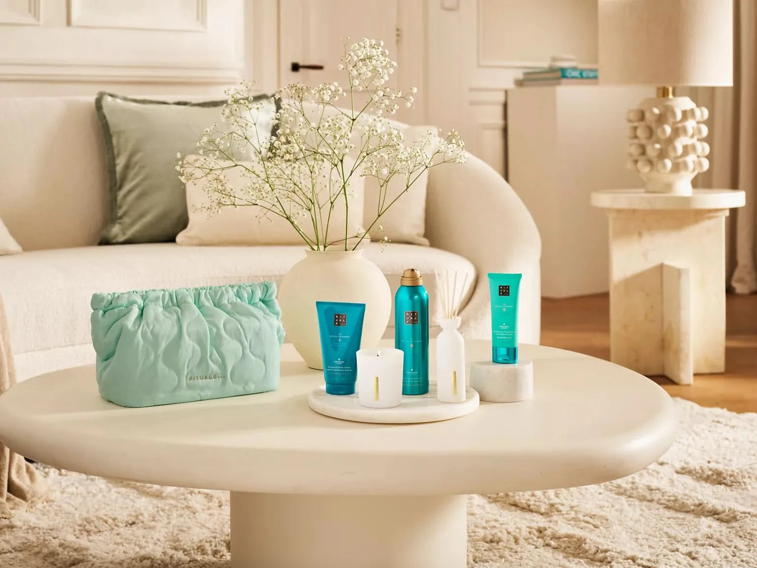 Zestaw upominkowy Rituals dla firm z kosmetykami i turkusową kosmetyczką na białym stoliku