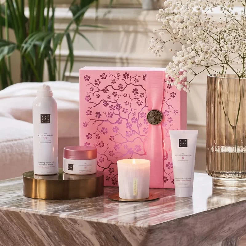 Zestaw prezentowy Rituals Sakura z różowym pudełkiem, świecą i kosmetykami na marmurowym stole